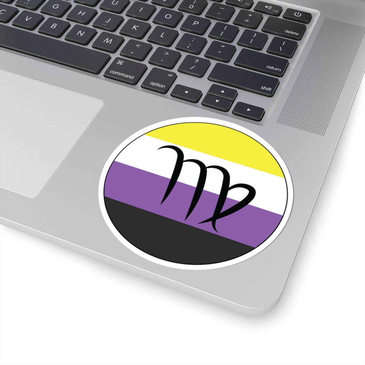 Close-up of the bottom right corner of a silver laptop featuring a 4 inch by 4 inch circular zodiac sticker with a centered Virgo glyph on a Nonbinary pride flag style background applied to the surface.