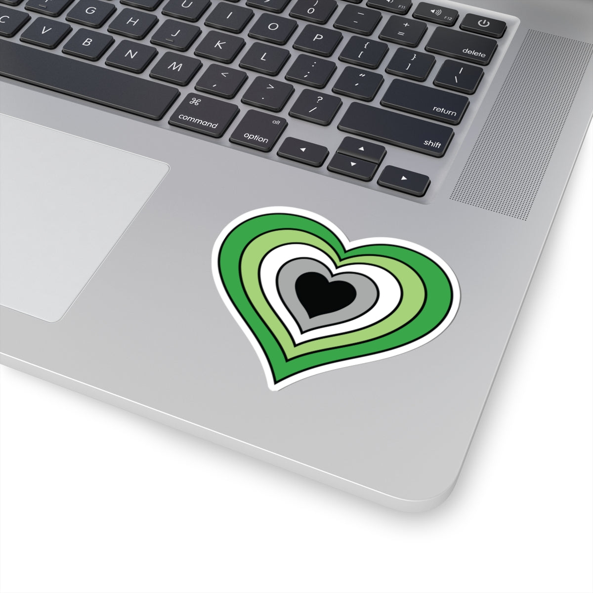 Close-up of the bottom right corner of a silver laptop featuring a 3 inch by 3 inch pride flag heart sticker in an Aromantic flag style applied to the surface.