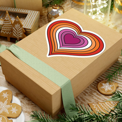 Gift box with a green ribbon on a festive table with cookies and decorations. Lesbian heart sticker centered on the box.