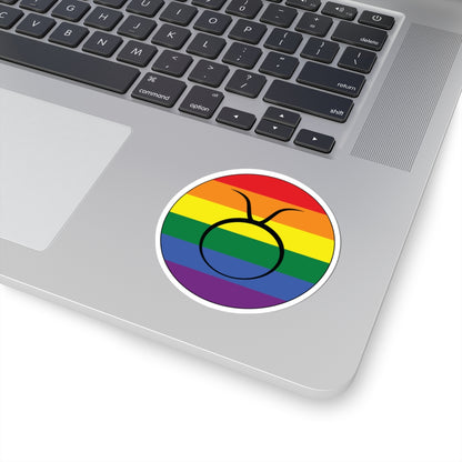 Close-up of the bottom right corner of a silver laptop featuring a 3 inch by 3 inch circular zodiac sticker with a centered Taurus glyph on a Rainbow pride flag style background applied to the surface.