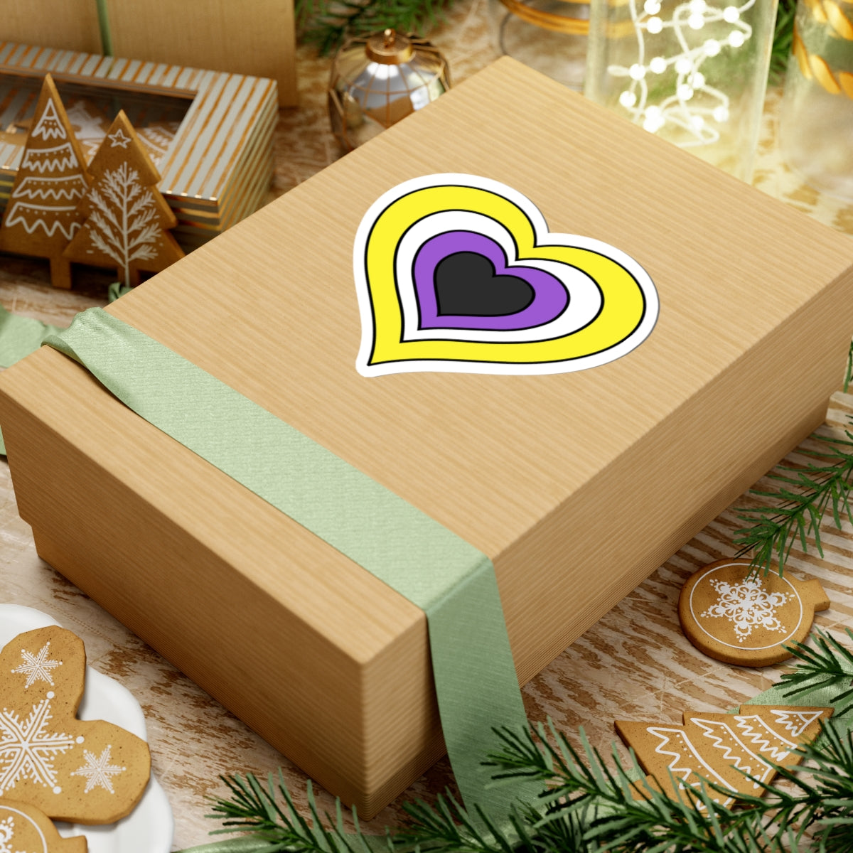 Gift box with a green ribbon on a festive background with cookies and Christmas decorations. Heart-shaped Nonbinary pride sticker centered on the box.