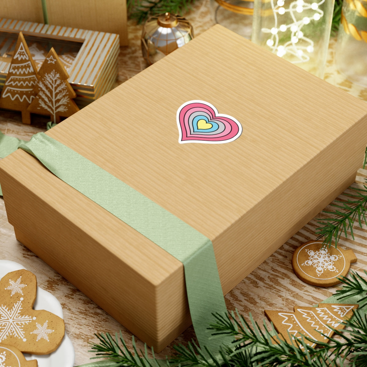 Gift box with a green ribbon on a festive background with cookies and Christmas decorations. Heart-shaped Genderflux pride sticker centered on the box.