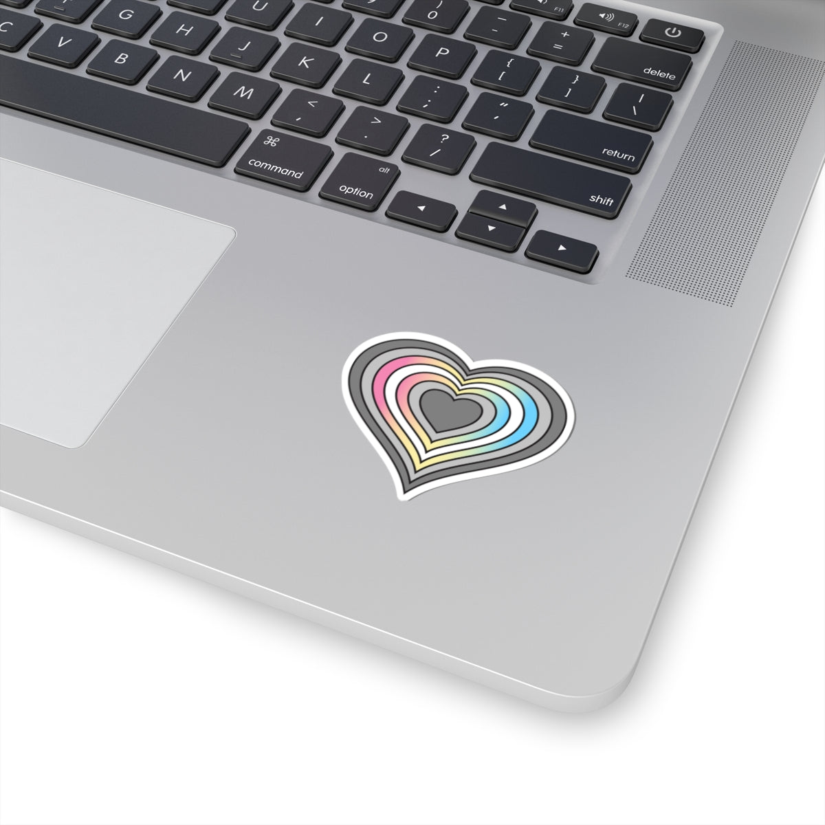 Close-up of the bottom right corner of a silver laptop featuring a 2 inch by 2 inch pride flag heart sticker in a Demifluid flag style applied to the surface.