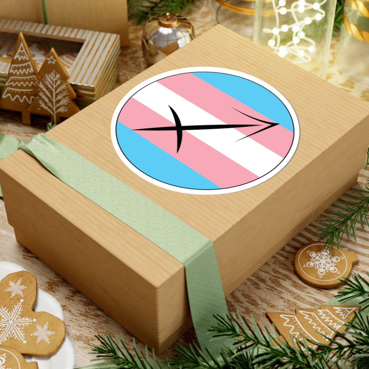 Gift box with a green ribbon on a festive background with cookies and Christmas decorations. Sagittarius Transgender pride sticker centered on the box.