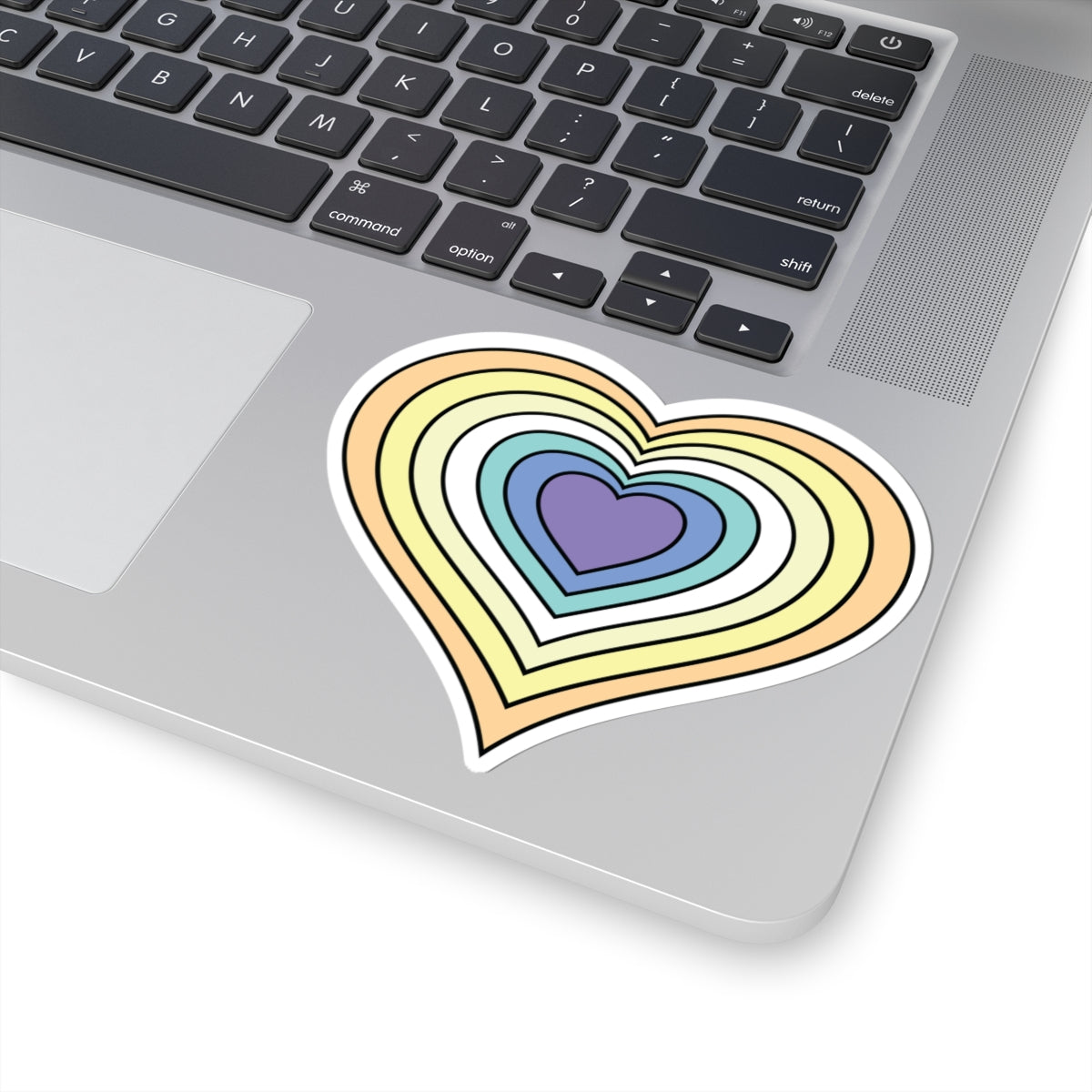 Close-up of the bottom right corner of a silver laptop featuring a 4 inch by 4 inch pride flag heart sticker in a Genderfaun flag style applied to the surface.