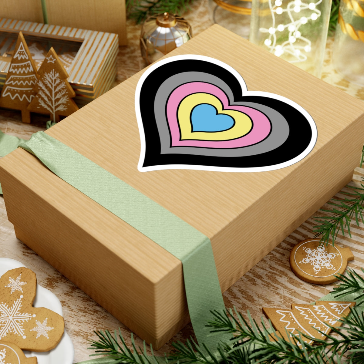 Gift box with a green ribbon on a festive background with cookies and Christmas decorations. Heart-shaped Polygender pride sticker centered on the box.