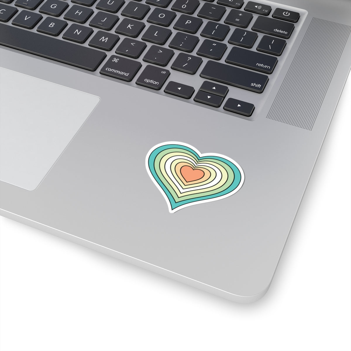 Close-up of the bottom right corner of a silver laptop featuring a 2 inch by 2 inch pride flag heart sticker in a Genderfloren flag style applied to the surface.