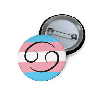 Front and back view of a circular transgender pride flag button featuring the Cancer zodiac symbol in black centered on the front.