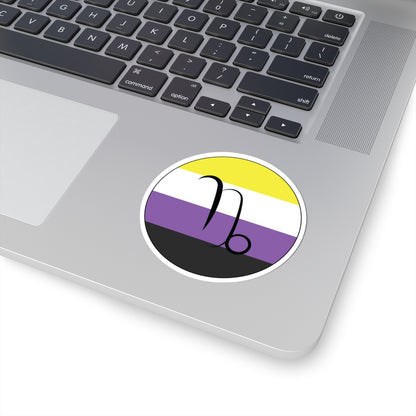 Close-up of the bottom right corner of a silver laptop featuring a 3 inch by 3 inch circular zodiac sticker with a centered Capricorn glyph on a Nonbinary pride flag style background applied to the surface.