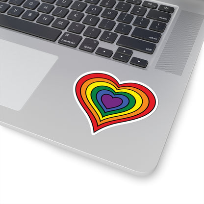 Close-up of the bottom right corner of a silver laptop featuring a 3 inch by 3 inch pride flag heart sticker in a rainbow pride flag style applied to the surface.