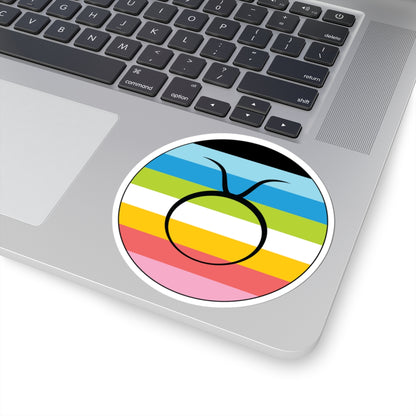 Close-up of the bottom right corner of a silver laptop featuring a 4 inch by 4 inch circular zodiac sticker with a centered Taurus glyph on a Queer pride flag style background applied to the surface.