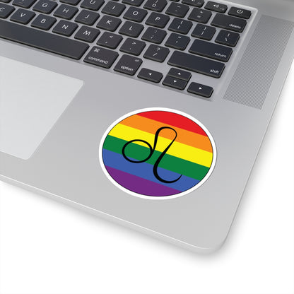 Close-up of the bottom right corner of a silver laptop featuring a 3 inch by 3 inch circular zodiac sticker with a centered Leo glyph on a Rainbow pride flag style background applied to the surface.