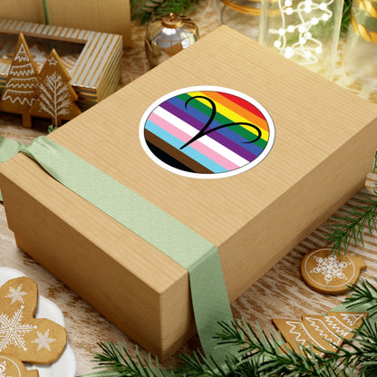 Gift box with a green ribbon on a festive background with cookies and Christmas decorations. Aires Progress pride sticker centered on the box.