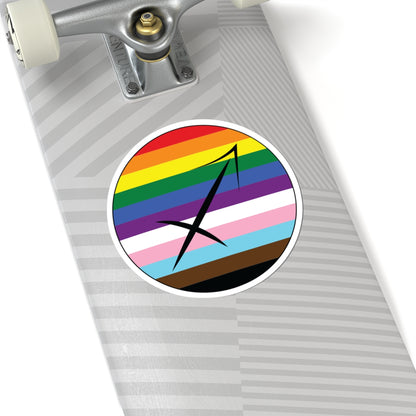 Close-up of the bottom of a silver skateboard featuring a 6 inch by 6 inch circular zodiac sticker with a centered Sagittarius glyph on a progress pride flag style background applied to the surface.