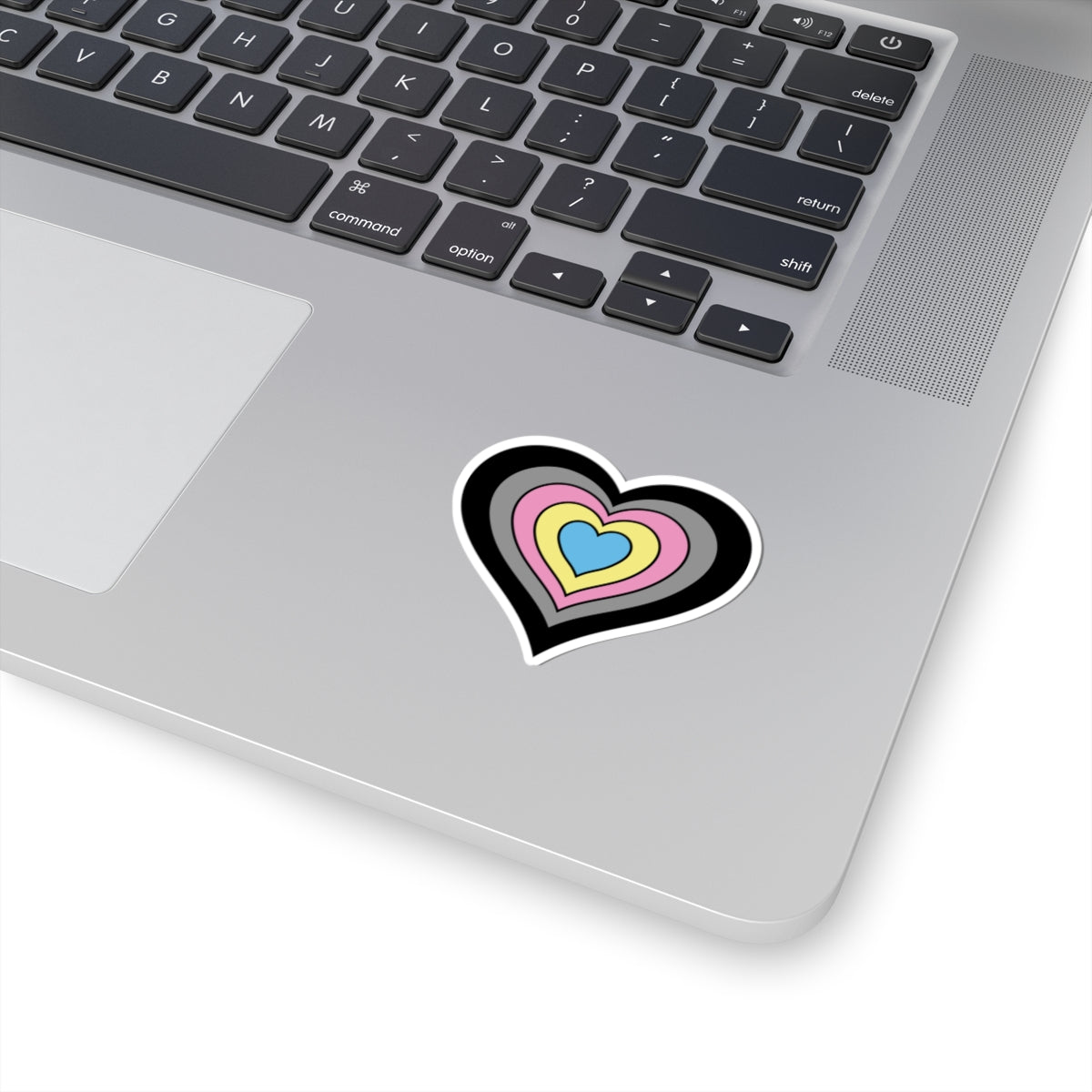Close-up of the bottom right corner of a silver laptop featuring a 2 inch by 2 inch pride flag heart sticker in a Polygender flag style applied to the surface.