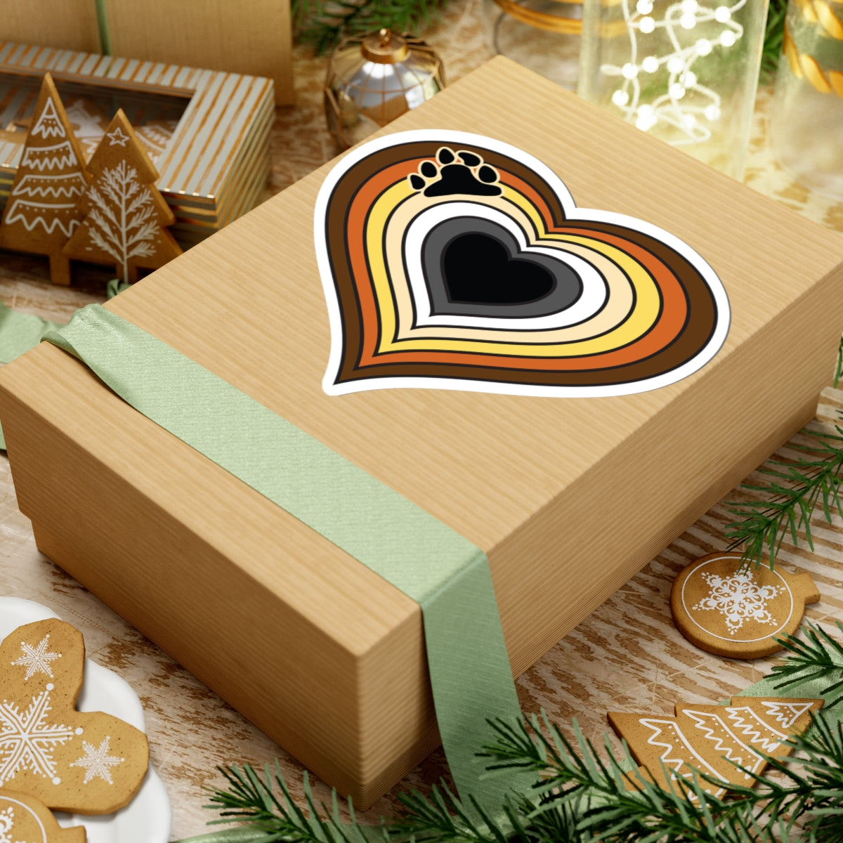 Gift box with a green ribbon on a festive background with cookies and Christmas decorations. Bear pride heart sticker centered on the box.