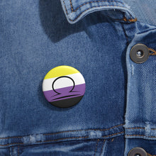 Close-up of a white circular pride button featuring the Libra zodiac glyph centered over a nonbinary pride flag background in yellow, white, purple, and black, attached to a blue denim jacket at the right chest with the button clearly visible.