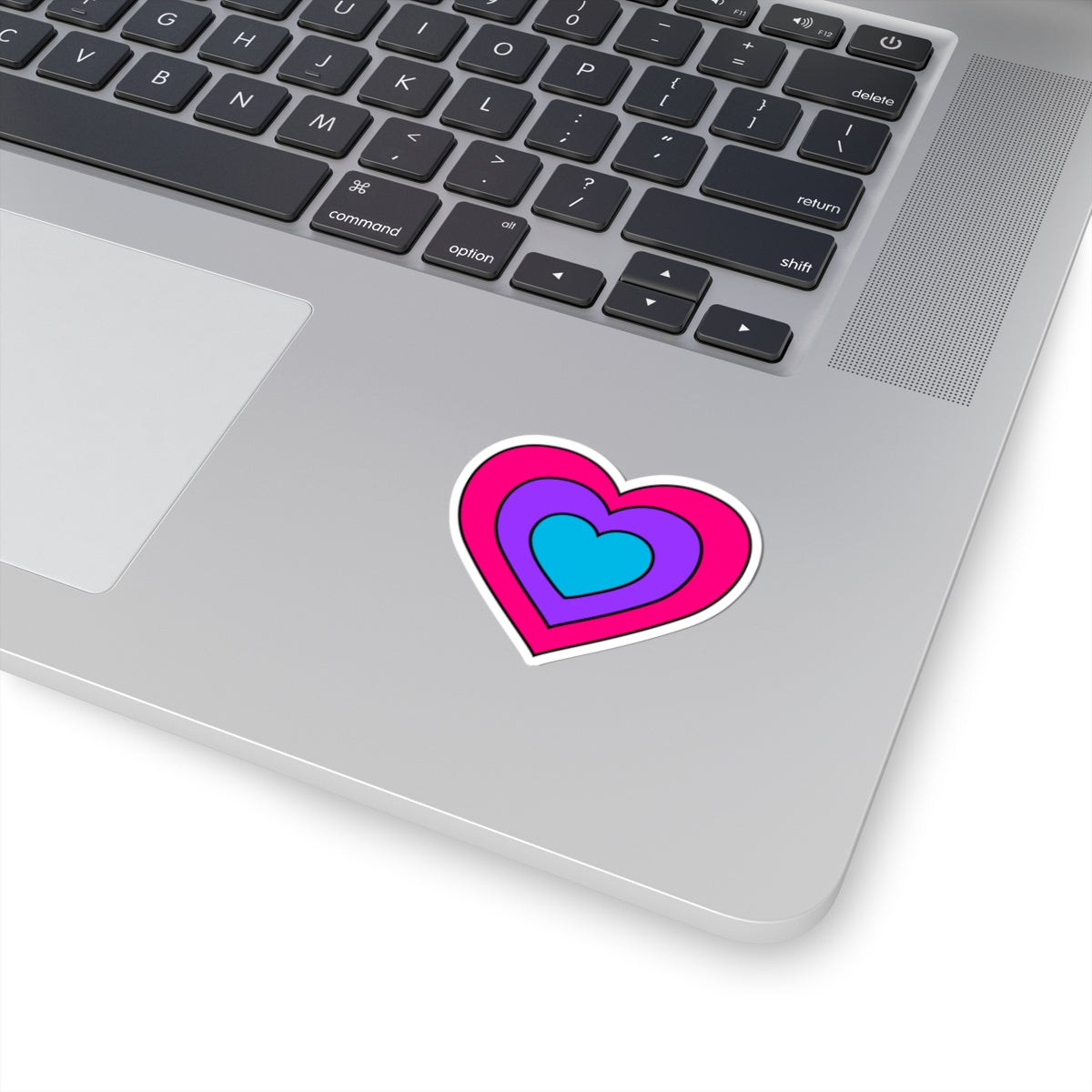 Close-up of the bottom right corner of a silver laptop featuring a 2 inch by 2 inch pride flag heart sticker in an Androgyne flag style applied to the surface.