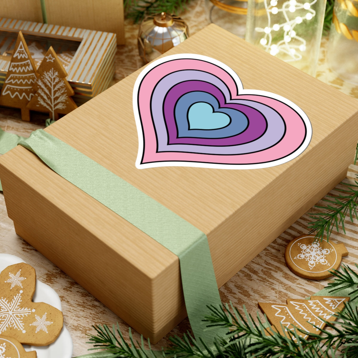 Gift box with a green ribbon on a festive background with cookies and Christmas decorations. Heart-shaped Omnigender pride sticker centered on the box.