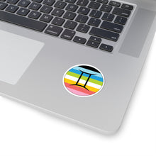 Close-up of the bottom right corner of a silver laptop featuring a 2 inch by 2 inch circular zodiac sticker with a centered Gemini glyph on a Queer pride flag style background applied to the surface.