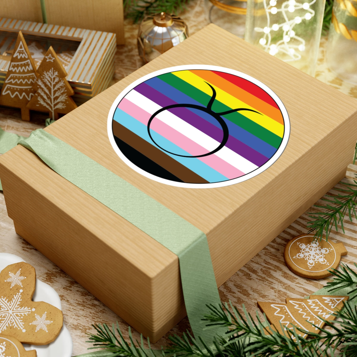 Gift box with a green ribbon on a festive background with cookies and Christmas decorations. Taurus Progress pride sticker centered on the box.
