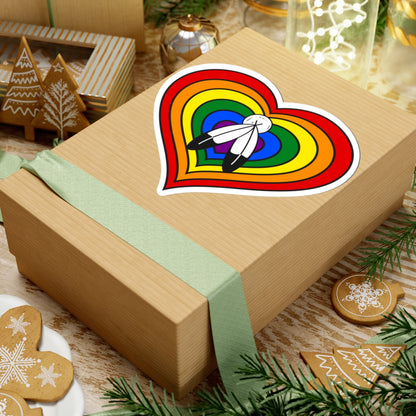 Gift box with a green ribbon on a festive background with cookies and Christmas decorations. Heart-shaped Two-Spirit pride sticker centered on the box.