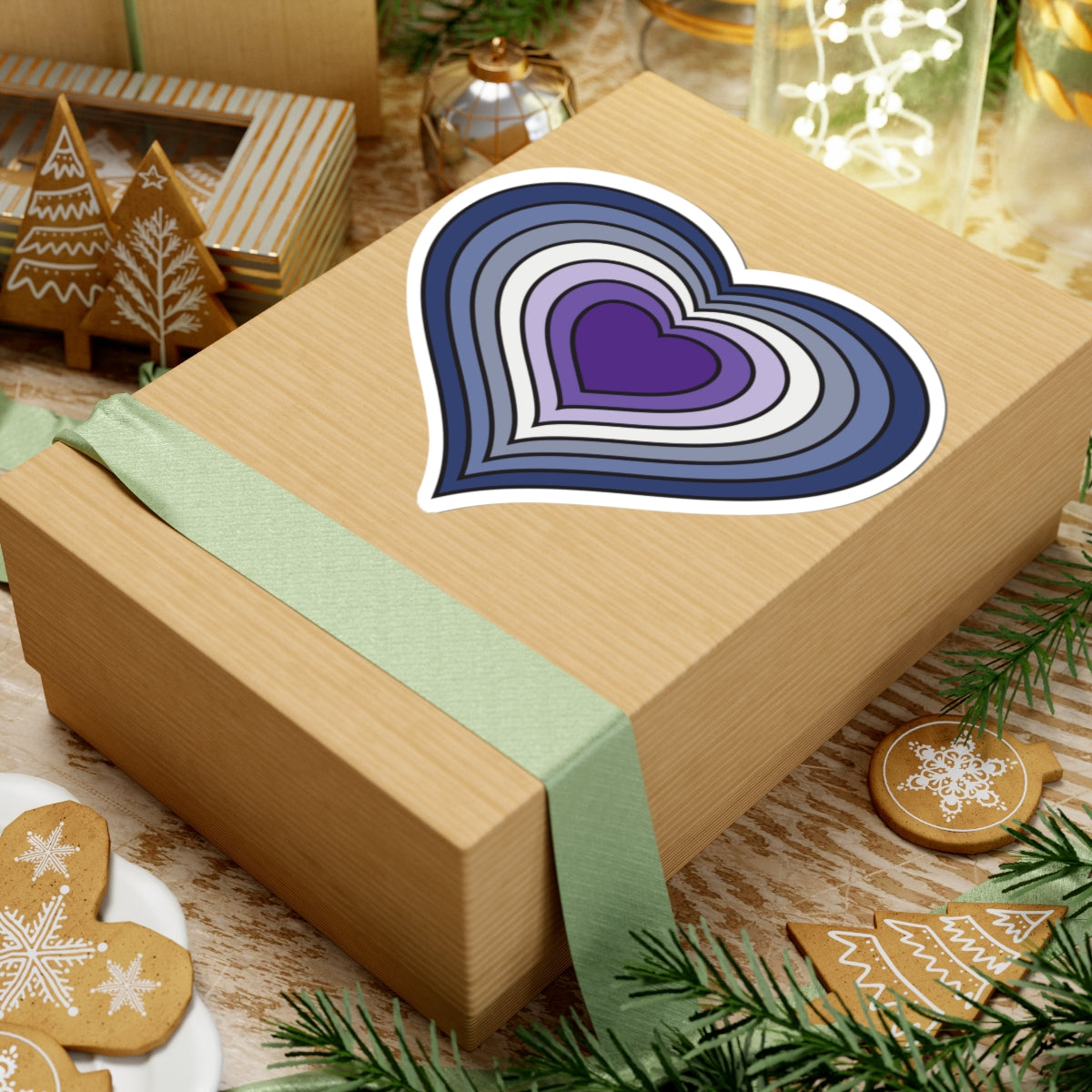 Gift box with a green ribbon on a festive background with cookies and Christmas decorations. Purple Butch pride heart sticker centered on the box.