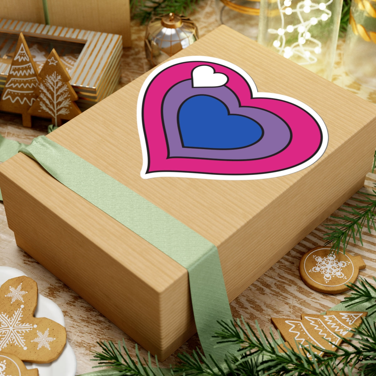 Gift box with a green ribbon on a festive background with cookies and Christmas decorations. Heart-shaped biromantic pride sticker centered on the box.
