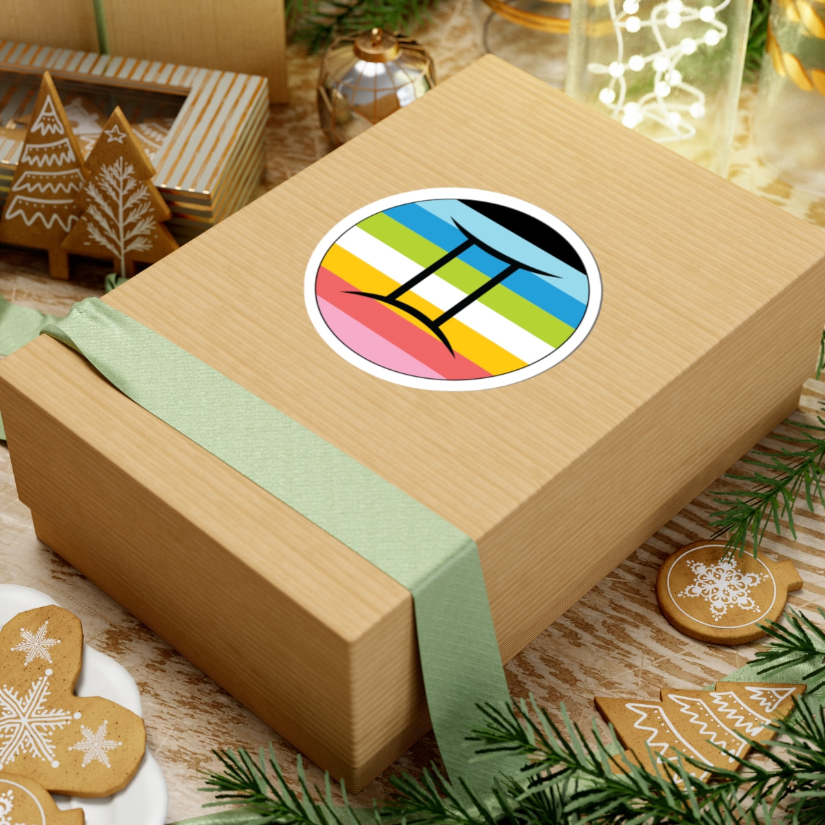 Gift box with a green ribbon on a festive background with cookies and Christmas decorations. Gemini Queer pride sticker centered on the box.