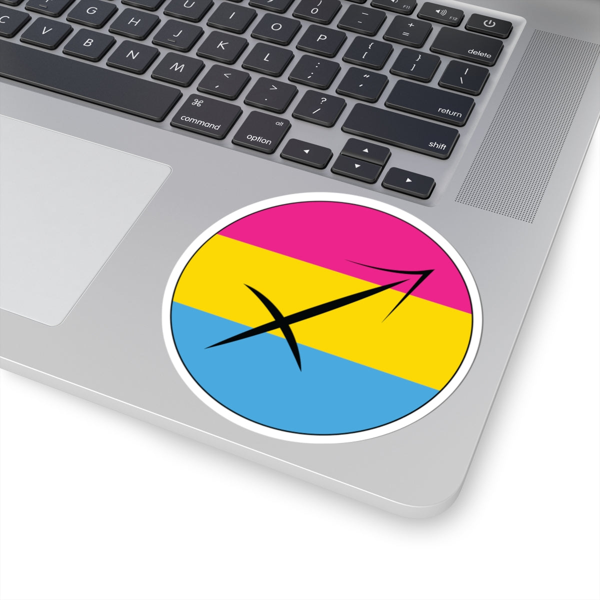 Close-up of the bottom right corner of a silver laptop featuring a 4 inch by 4 inch circular zodiac sticker with a centered Sagittarius glyph on a Pansexual pride flag style background applied to the surface.