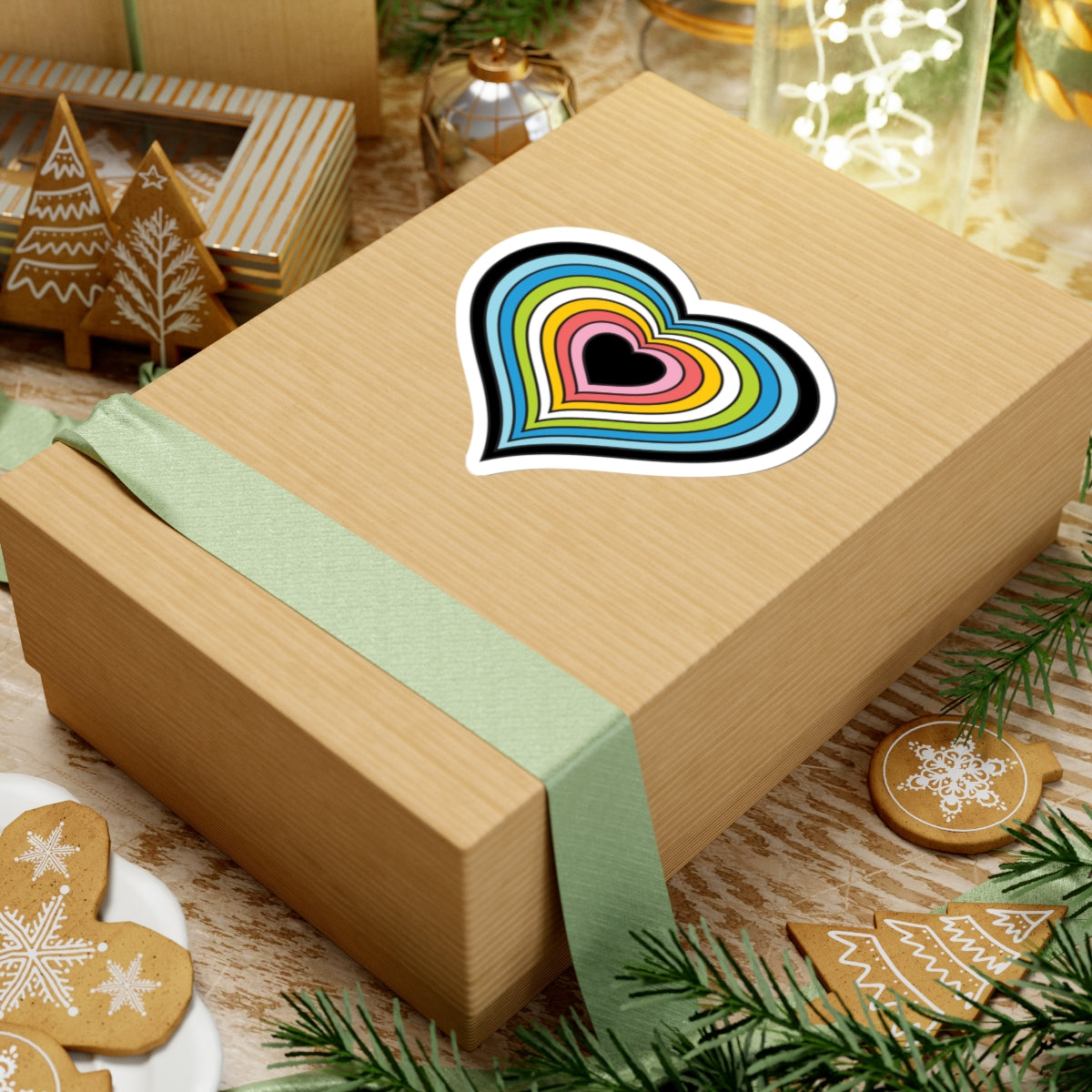 Gift box with a green ribbon on a festive background with cookies and Christmas decorations. Heart-shaped Queer pride sticker centered on the box.