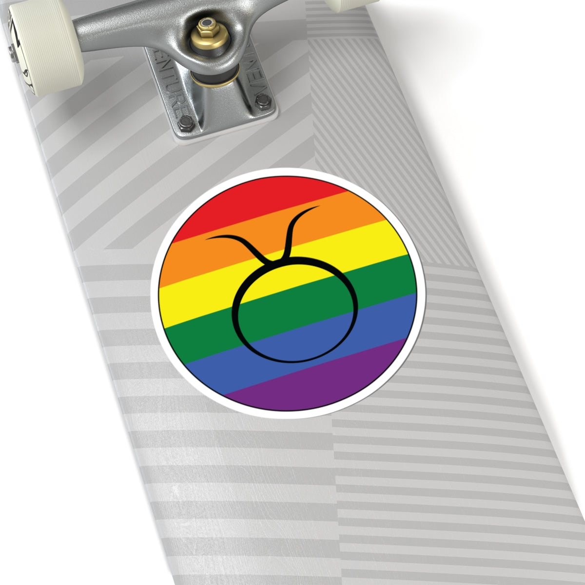 Close-up of the bottom of a silver skateboard featuring a 6 inch by 6 inch circular zodiac sticker with a centered Taurus glyph on a Rainbow pride flag style background applied to the surface.