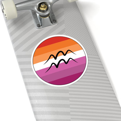 Close-up of the bottom of a silver skateboard featuring a 6 inch by 6 inch circular zodiac sticker with a centered Aquarius glyph on a Lesbian pride flag style background applied to the surface.