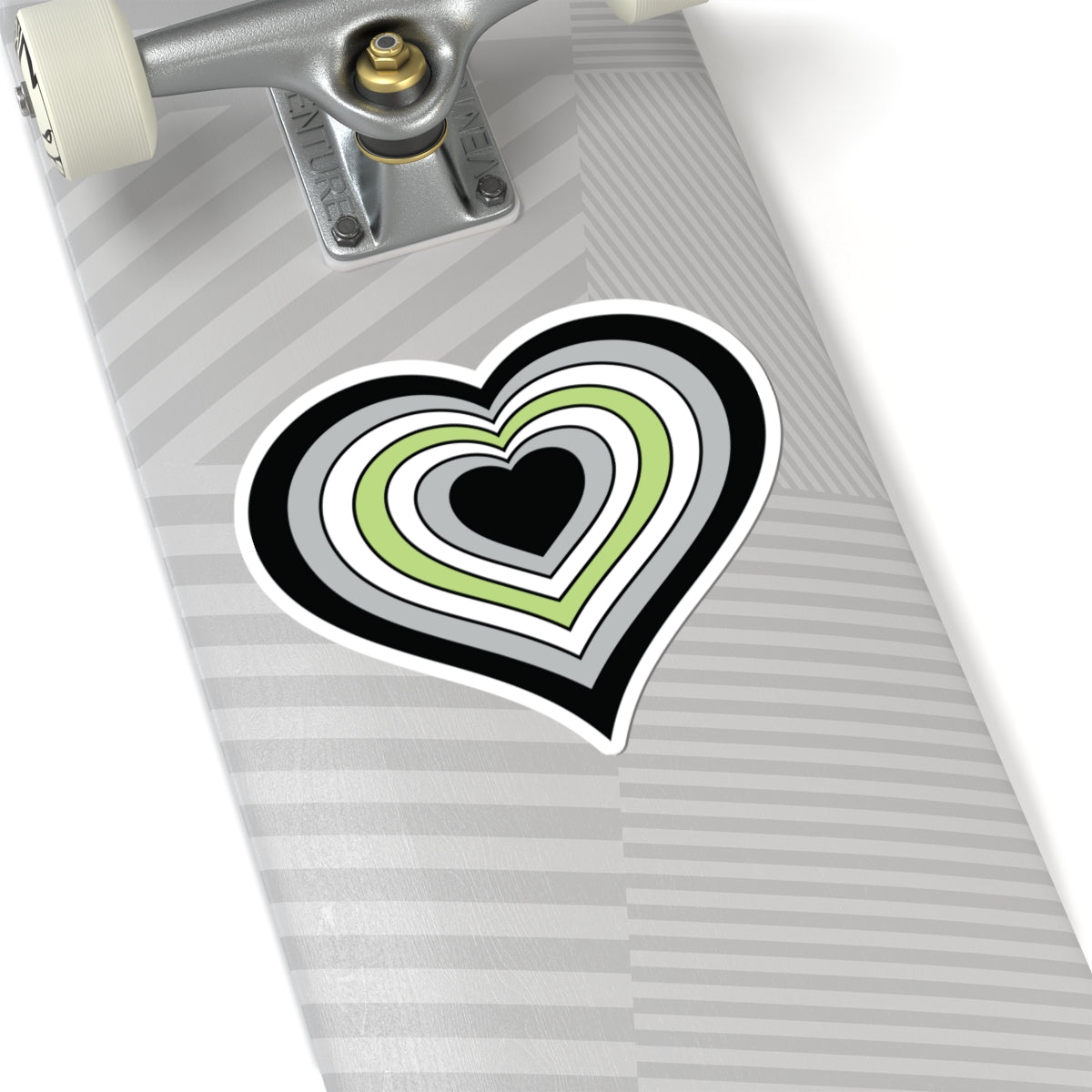 Close-up of the bottom of a silver skateboard featuring a 6 inch by 6 inch pride flag heart sticker in a Agender flag style applied to the surface.