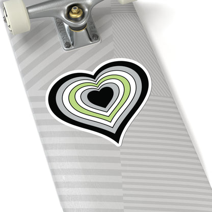 Close-up of the bottom of a silver skateboard featuring a 6 inch by 6 inch pride flag heart sticker in a Agender flag style applied to the surface.