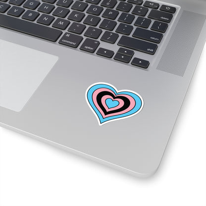 Close-up of the bottom right corner of a silver laptop featuring a 2 inch by 2 inch pride flag heart sticker in a Black Trans flag style applied to the surface.