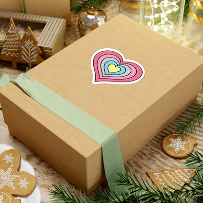 Gift box with a green ribbon on a festive background with cookies and Christmas decorations. Heart-shaped Genderflux pride sticker centered on the box.