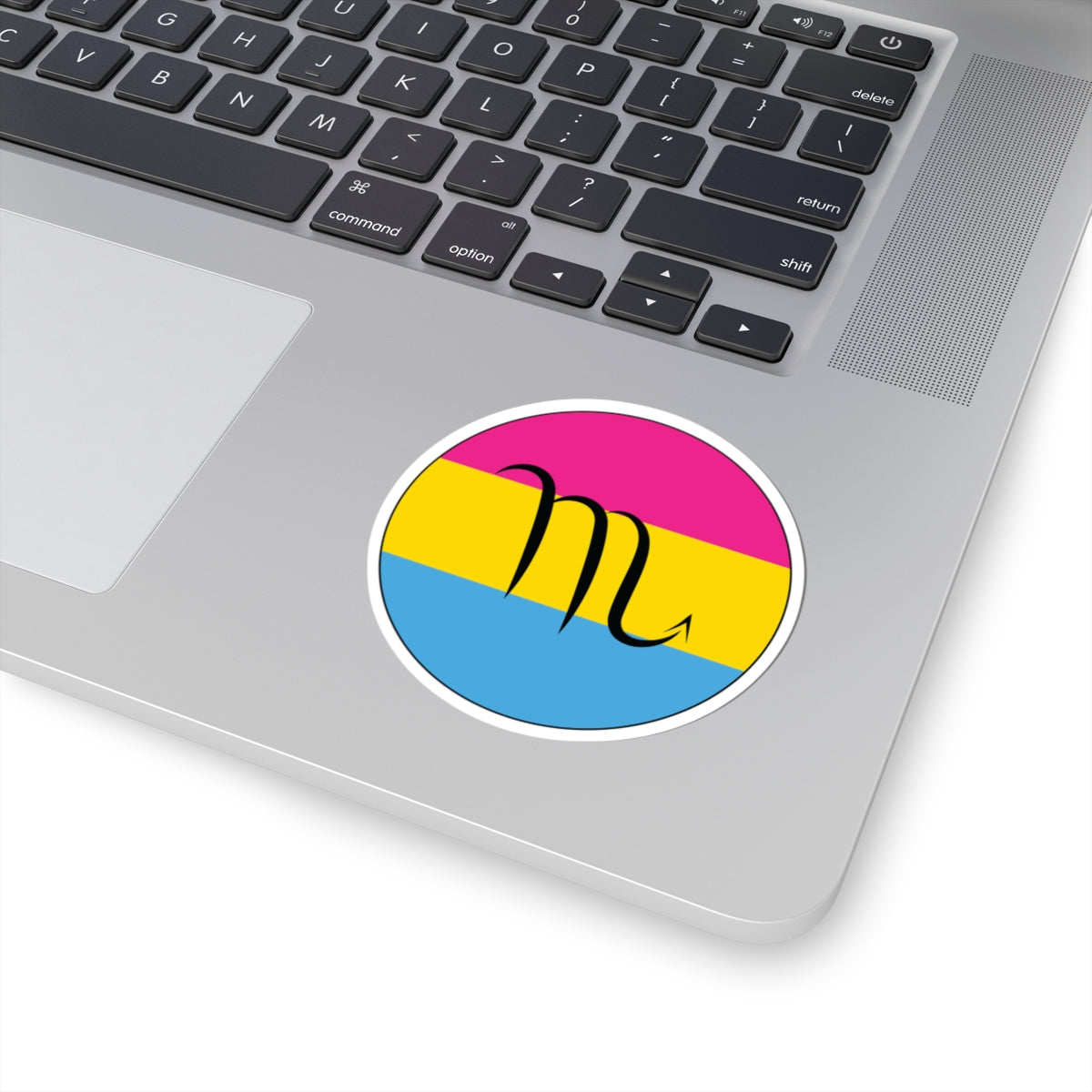 Close-up of the bottom right corner of a silver laptop featuring a 3 inch by 3 inch circular zodiac sticker with a centered Scorpio glyph on a Pansexual pride flag style background applied to the surface.