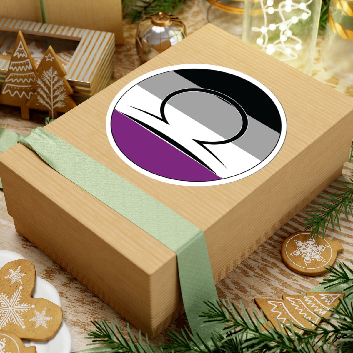 Gift box with a green ribbon on a festive background with cookies and Christmas decorations. Libra Asexual pride sticker centered on the box.