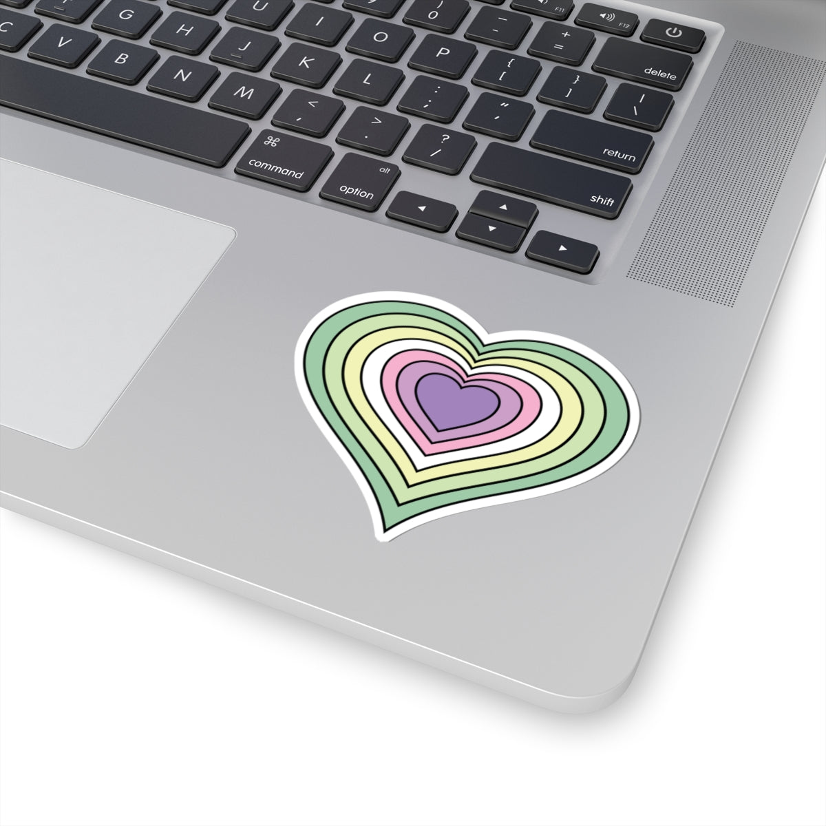 Close-up of the bottom right corner of a silver laptop featuring a 3 inch by 3 inch pride flag heart sticker in a Genderfae flag style applied to the surface.