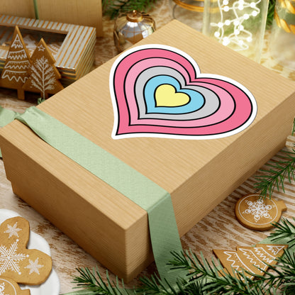 Gift box with a green ribbon on a festive background with cookies and Christmas decorations. Heart-shaped Genderflux pride sticker centered on the box.