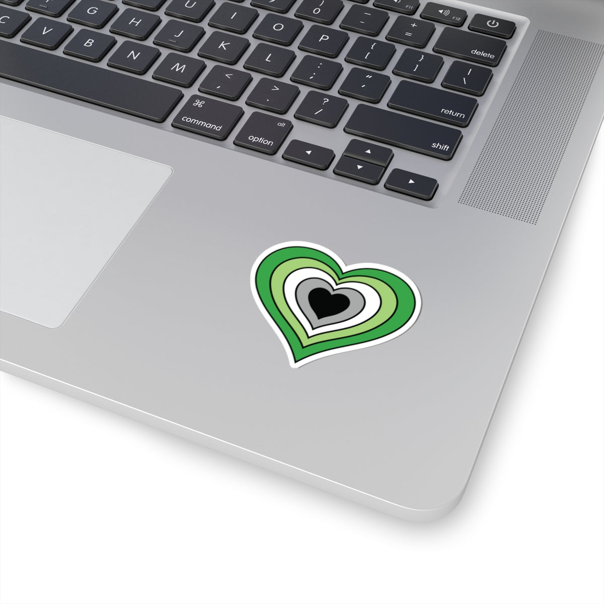 Close-up of the bottom right corner of a silver laptop featuring a 2 inch by 2 inch pride flag heart sticker in an Aromantic flag style applied to the surface.