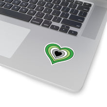 Close-up of the bottom right corner of a silver laptop featuring a 2 inch by 2 inch pride flag heart sticker in an Aromantic flag style applied to the surface.