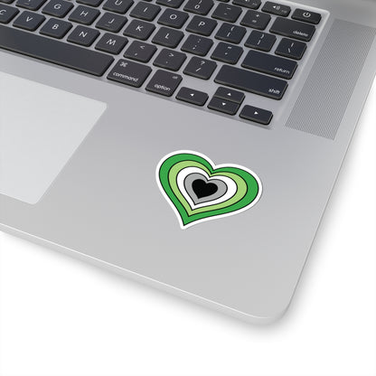 Close-up of the bottom right corner of a silver laptop featuring a 2 inch by 2 inch pride flag heart sticker in an Aromantic flag style applied to the surface.