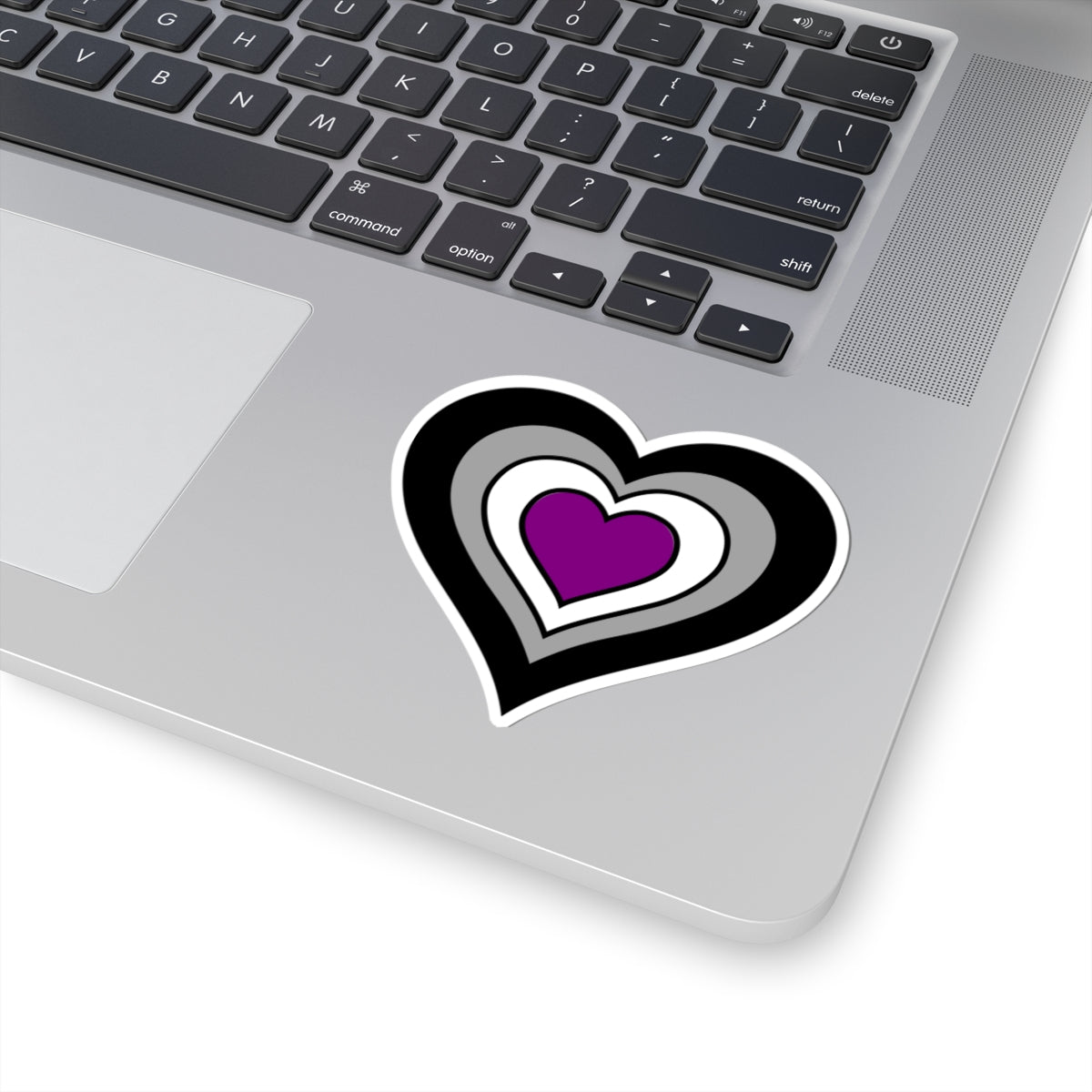 Close-up of the bottom right corner of a silver laptop featuring a 3 inch by 3 inch pride flag heart sticker in an Asexual flag style applied to the surface.