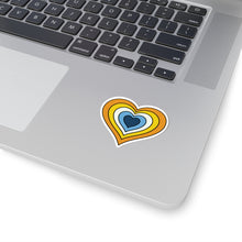 Close-up of the bottom right corner of a silver laptop featuring a 2 inch by 2 inch pride flag heart sticker in an Aroace flag style applied to the surface.