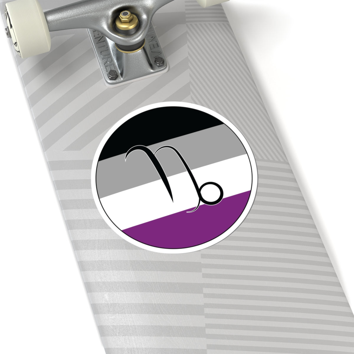 Close-up of the bottom of a silver skateboard featuring a 6 inch by 6 inch circular zodiac sticker with a centered Capricorn glyph on an Asexual pride flag style background applied to the surface.