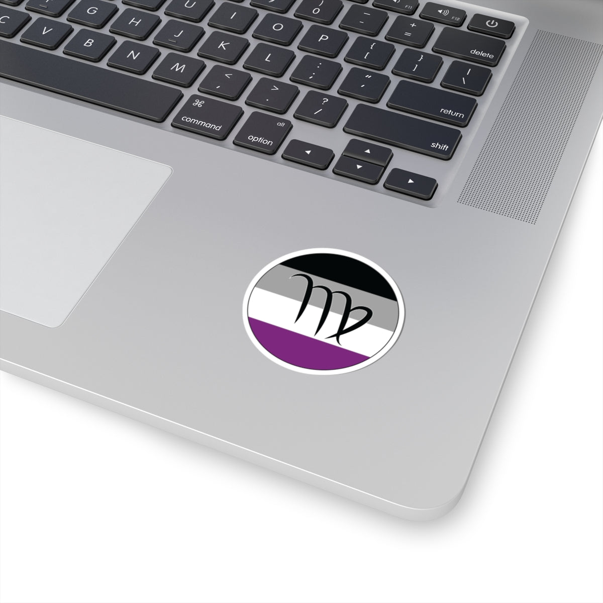 Close-up of the bottom right corner of a silver laptop featuring a 2 inch by 2 inch circular zodiac sticker with a centered Virgo glyph on an Asexual pride flag style background applied to the surface.
