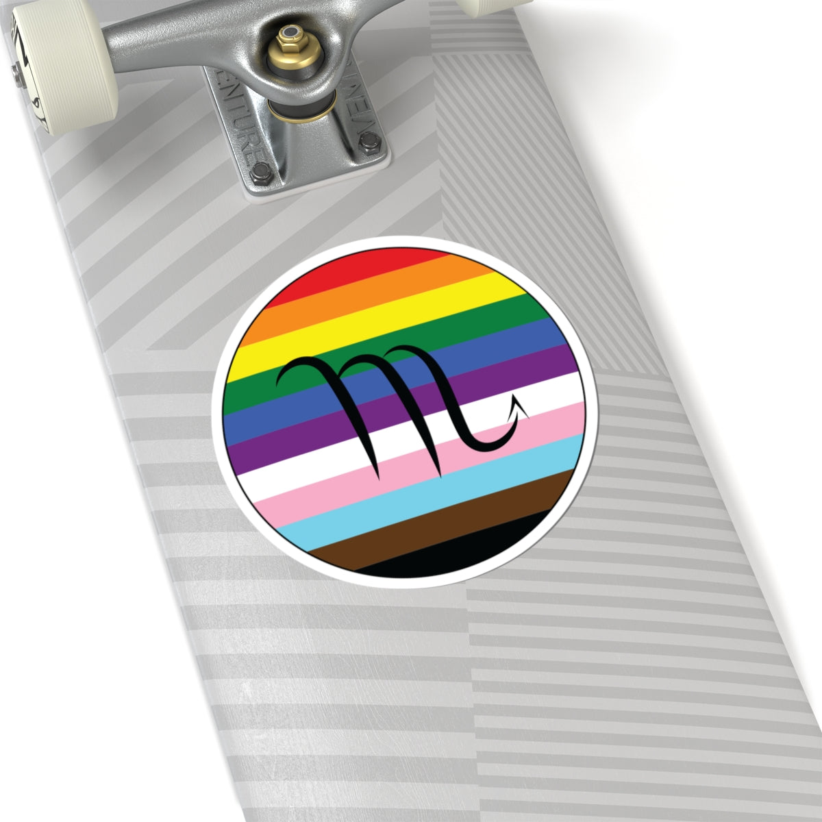 Close-up of the bottom of a silver skateboard featuring a 6 inch by 6 inch circular zodiac sticker with a centered Scorpio glyph on a progress pride flag style background applied to the surface.