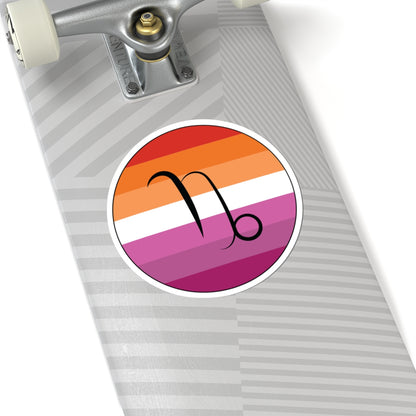 Close-up of the bottom of a silver skateboard featuring a 6 inch by 6 inch circular zodiac sticker with a centered Capricorn glyph on a Lesbian pride flag style background applied to the surface.